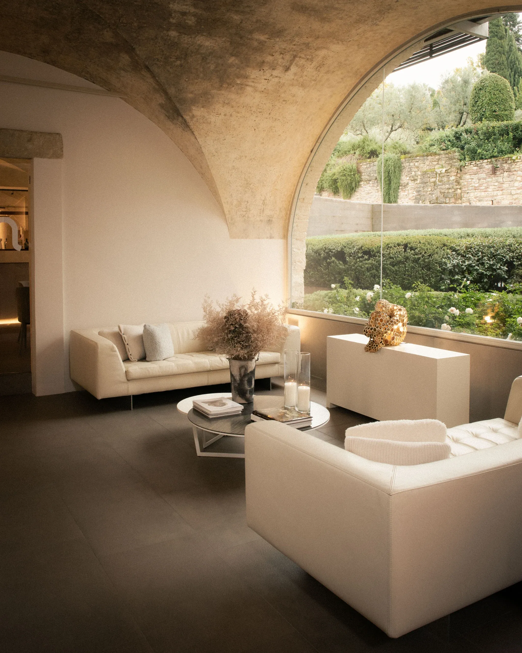 Vaulted lounge interior with white sofas and arched window onto garden alternative framing
