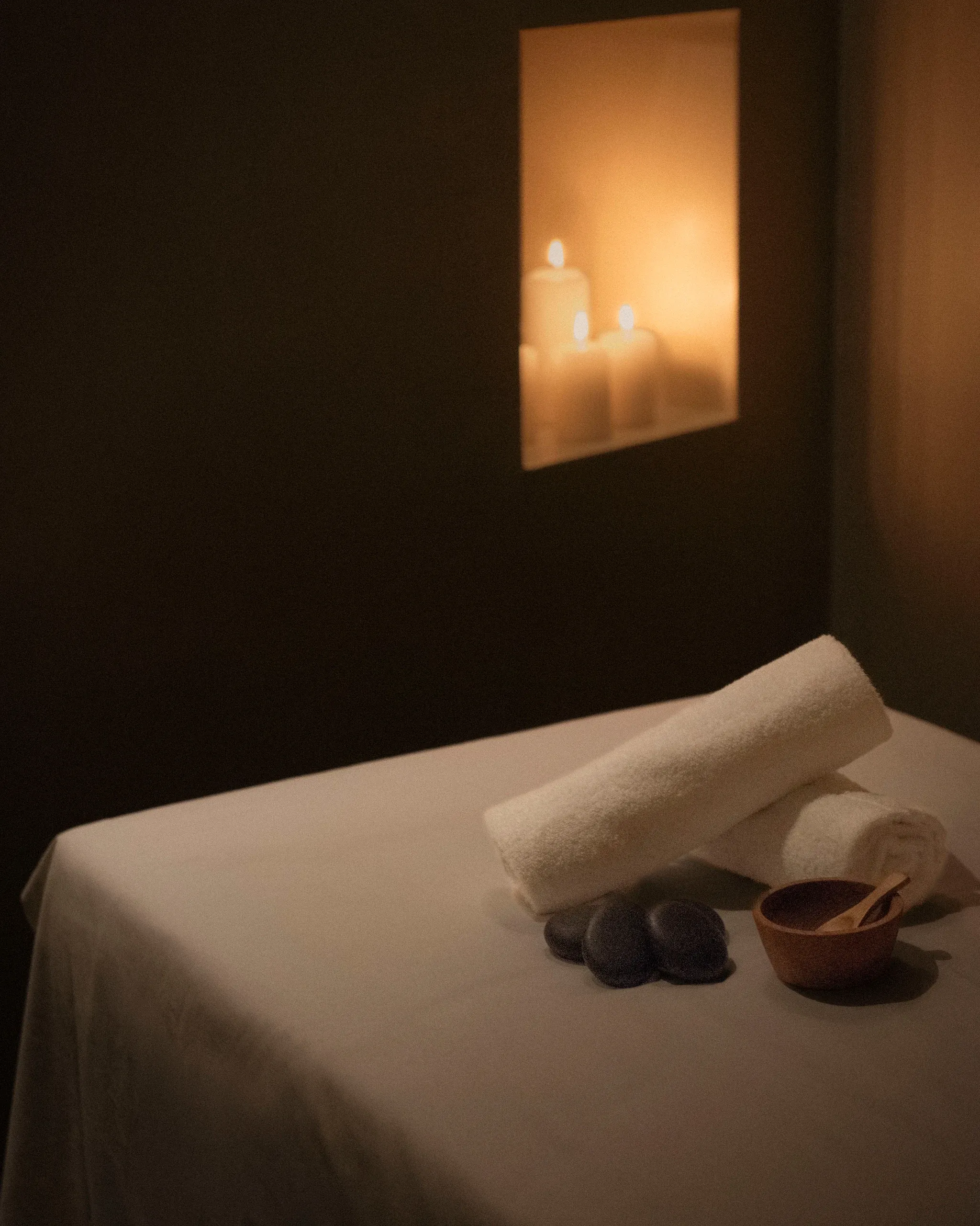 Massage table detail with rolled towels, hot stones, ceramic bowl and candle niche