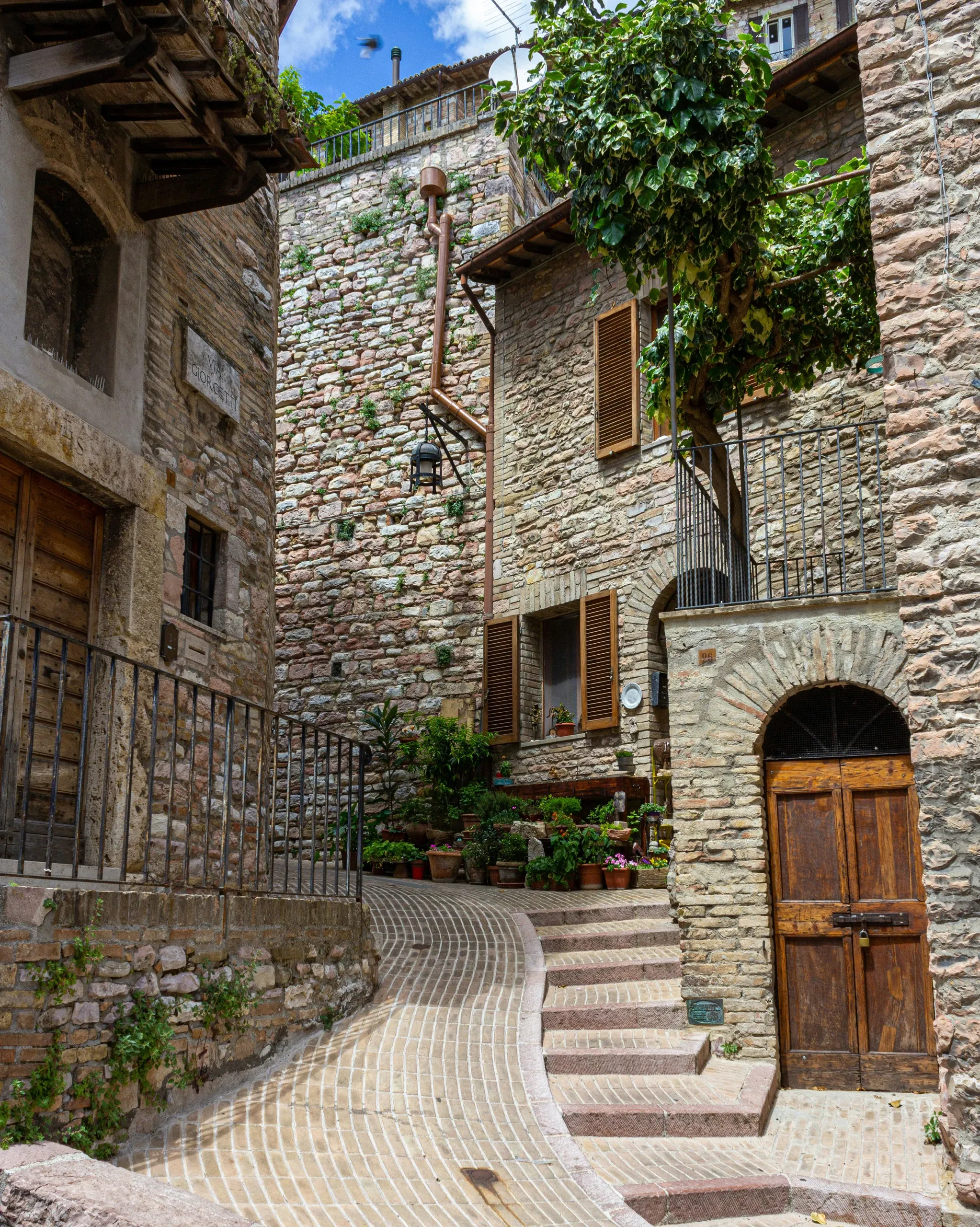 Stone alley in Assisi with arched wooden door and flowering plants